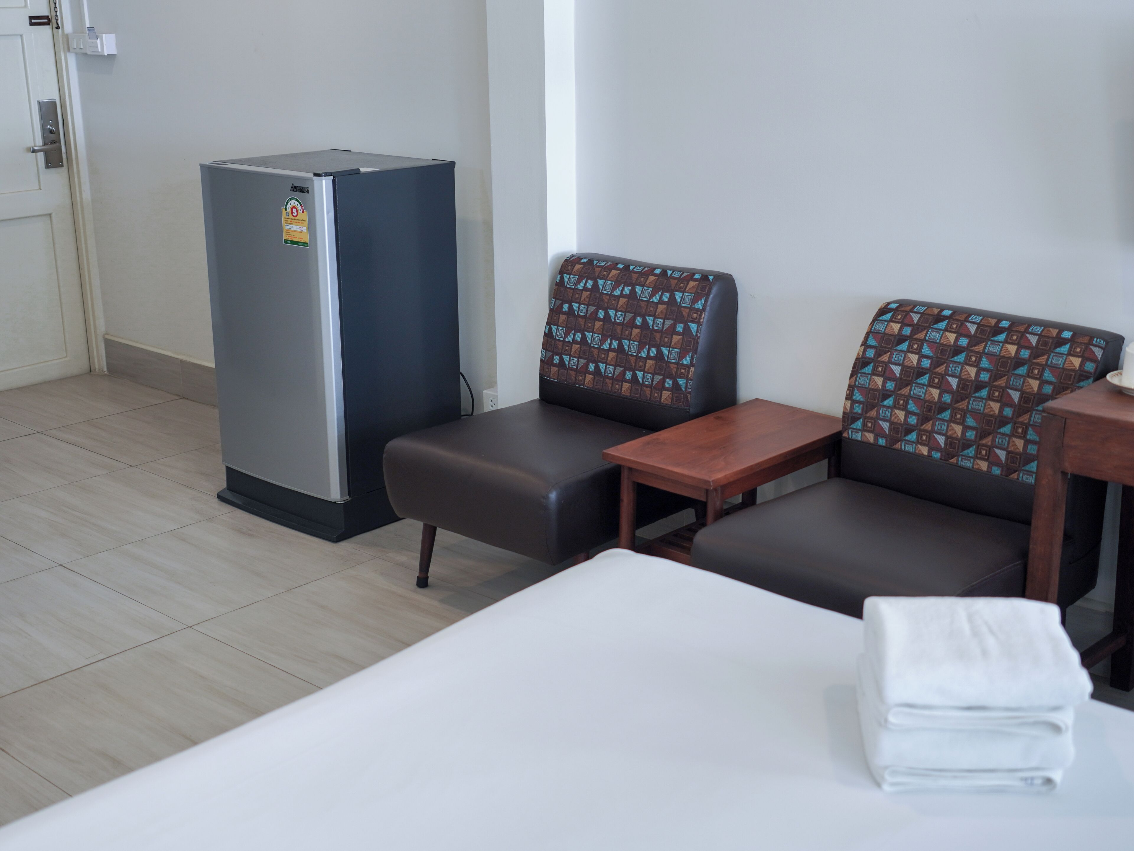 A hotel room with a bed, a small table, a sofa, and a refrigerator.