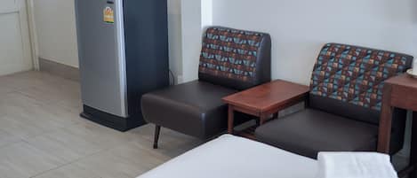A hotel room with a bed, a small table, a sofa, and a refrigerator.