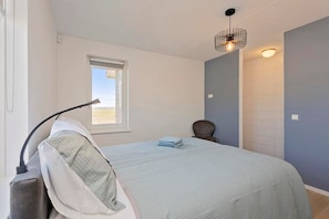 Une chambre à coucher comprenant un lit, une chaise, une fenêtre et un luminaire fixé au mur.