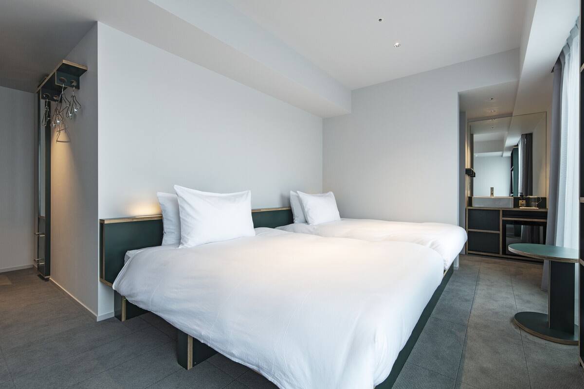 A modern hotel room with two beds, a built-in TV, a small seating area, and a large mirror.