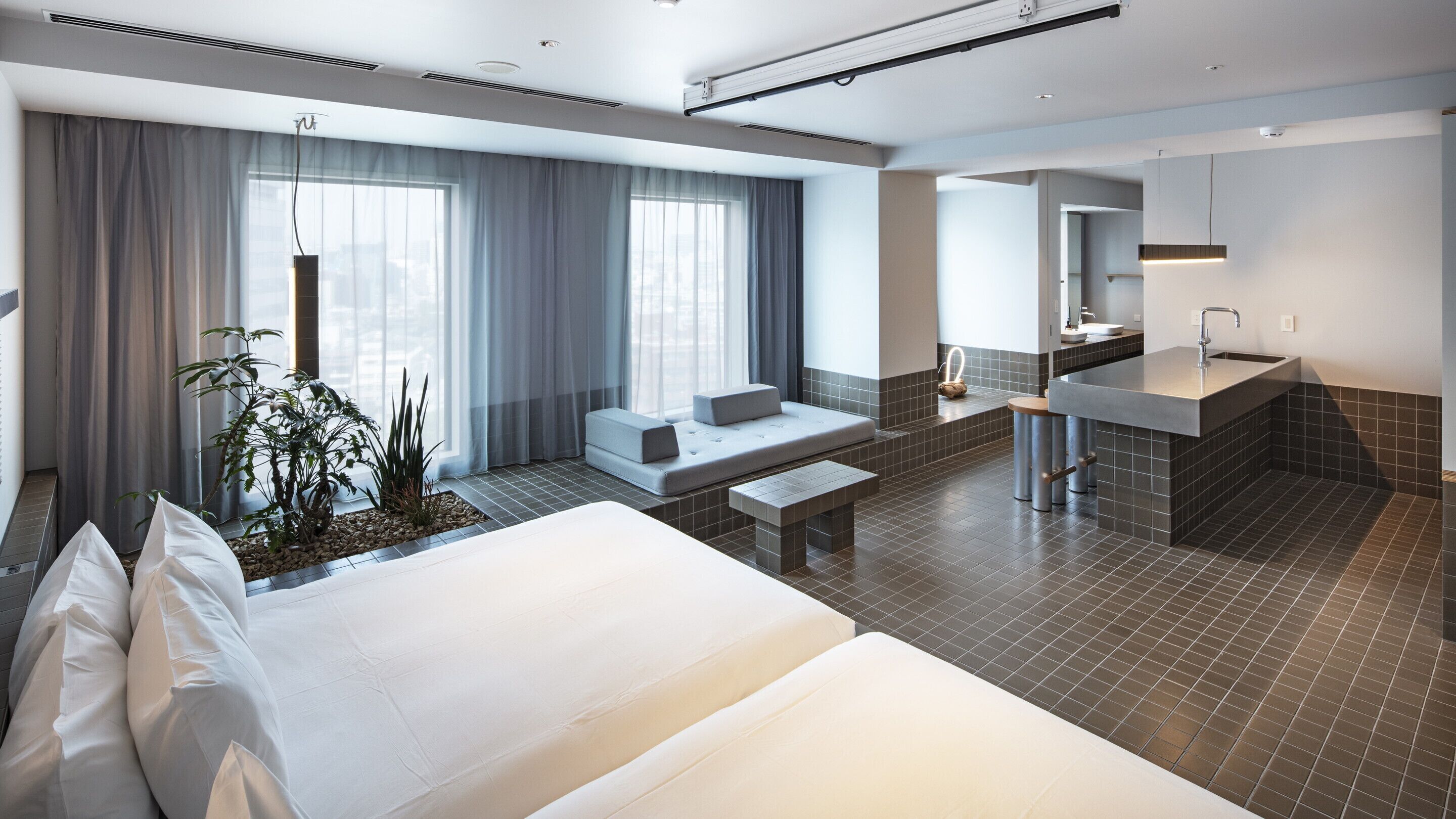 Una habitación de hotel moderna con una cama grande, un área de descanso con cojines, una mesita y un lavamanos con espejo.