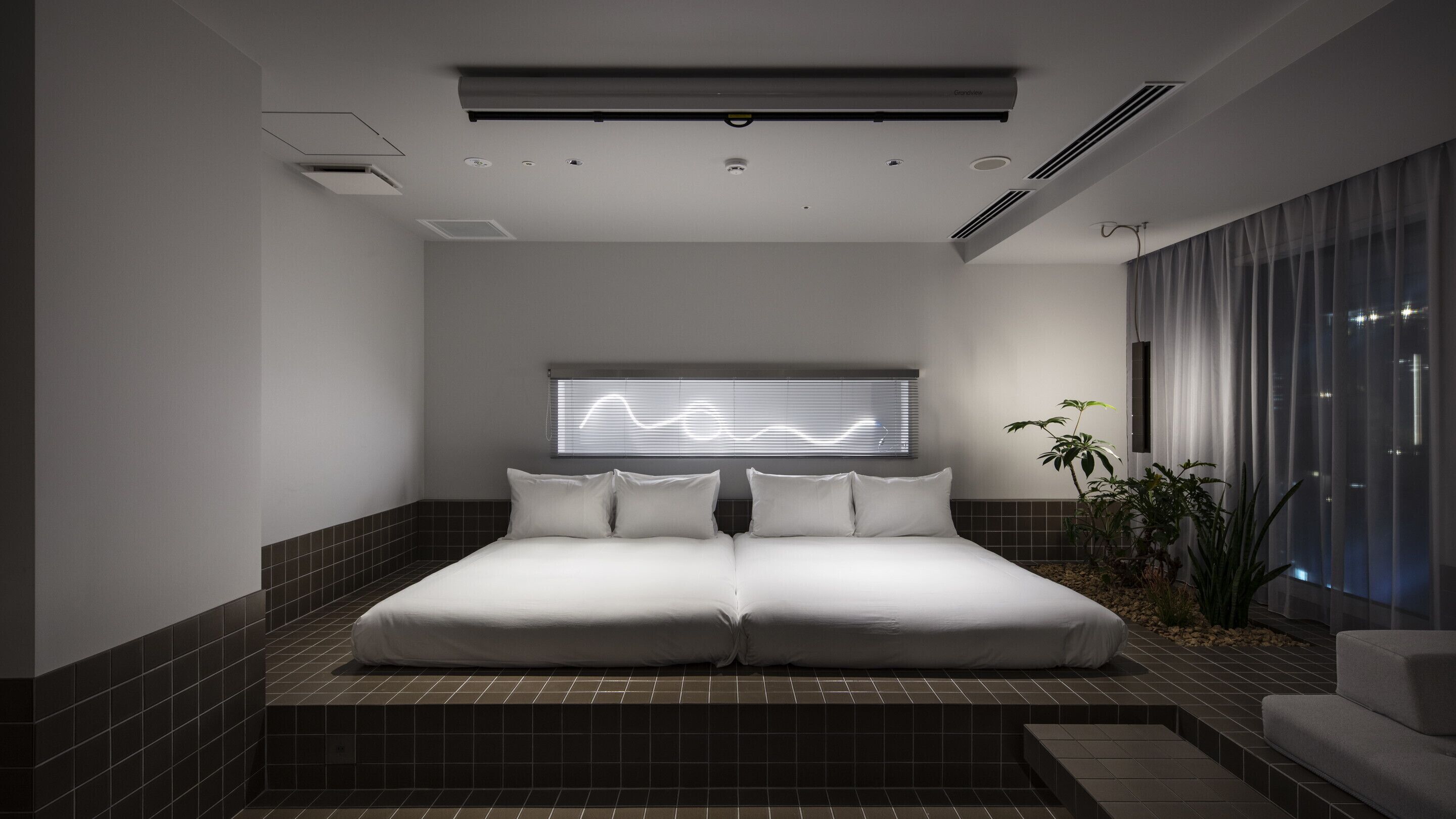 A modern bedroom with a large bed, a wall-mounted air conditioning unit, and a window with blinds.
