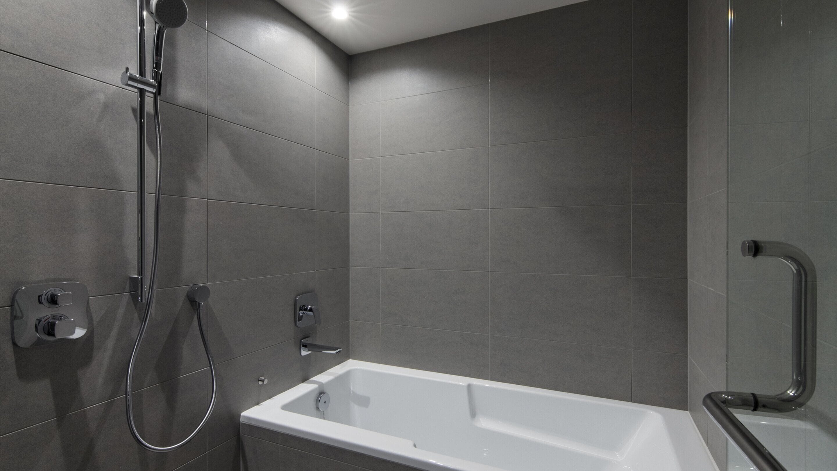 A modern bathroom with a bathtub, a shower, and a handrail.