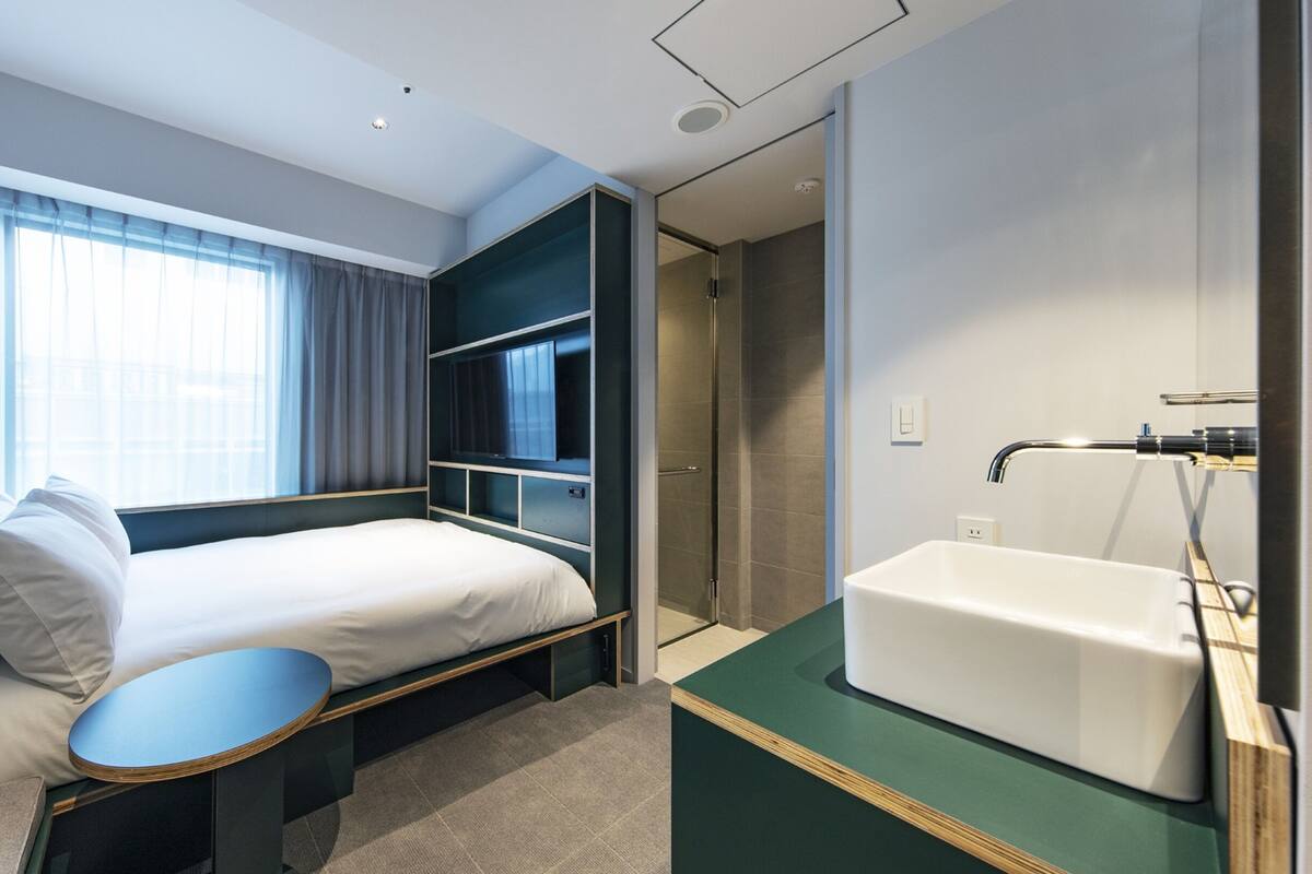 A hotel room with a bed, a small table, a TV, a shower, and a sink.