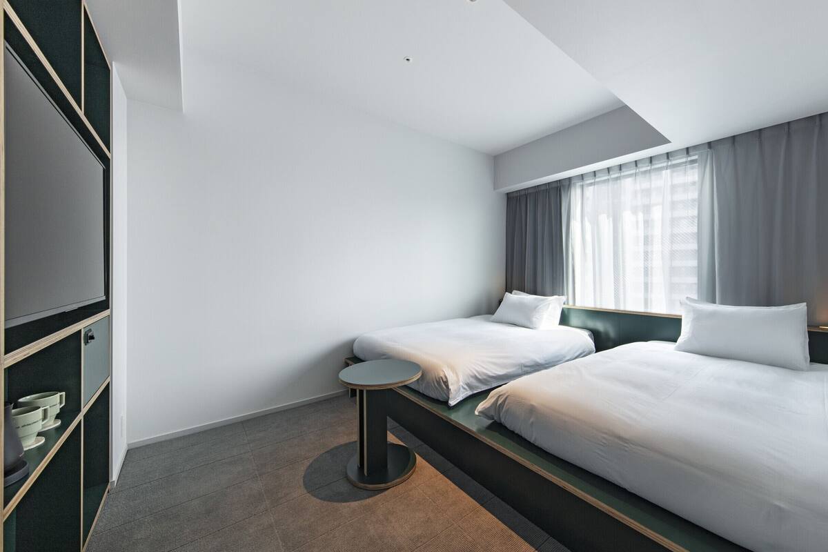 A hotel room with two beds, a small round table, a wardrobe, and a window with curtains.