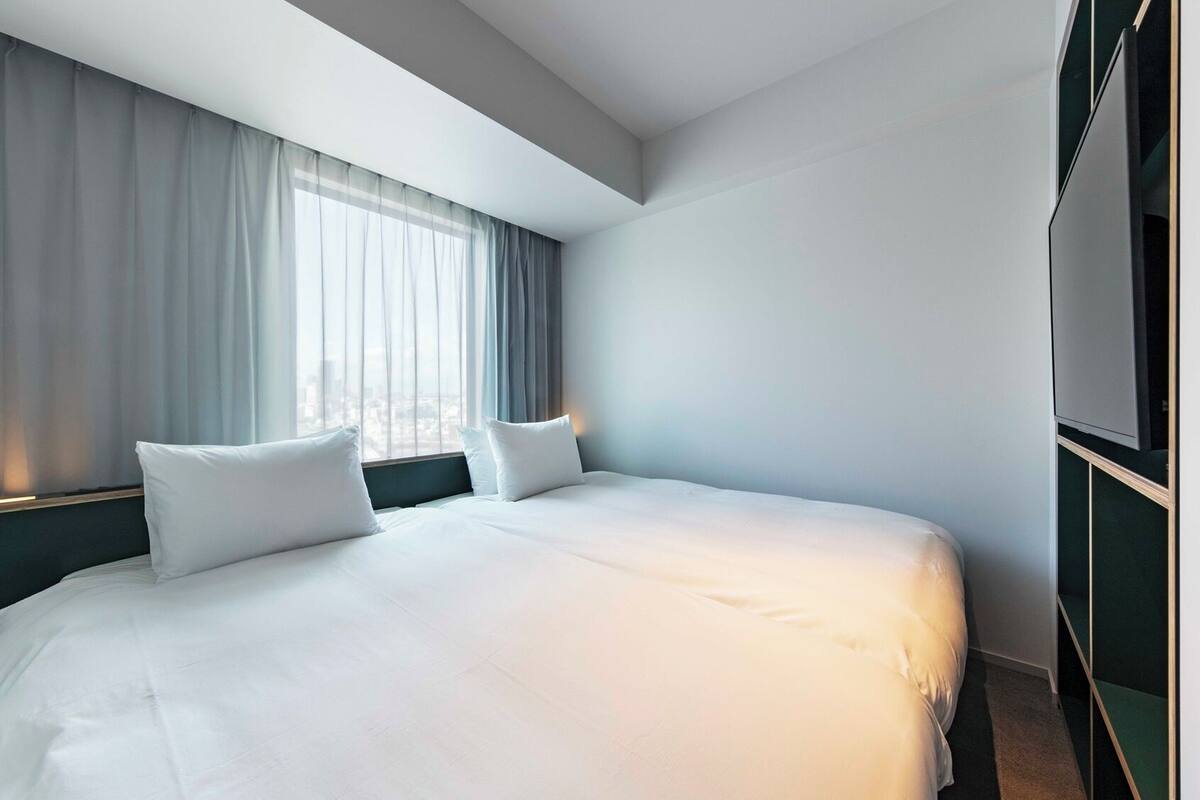 A hotel room with a large bed, two pillows, a nightstand, a TV, and a window with curtains.