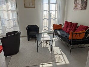 A modern living room with a black sofa, red and orange cushions, a black armchair, and a small table.