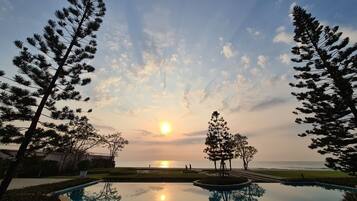 A pool reflecting trees and a sunset over the ocean.