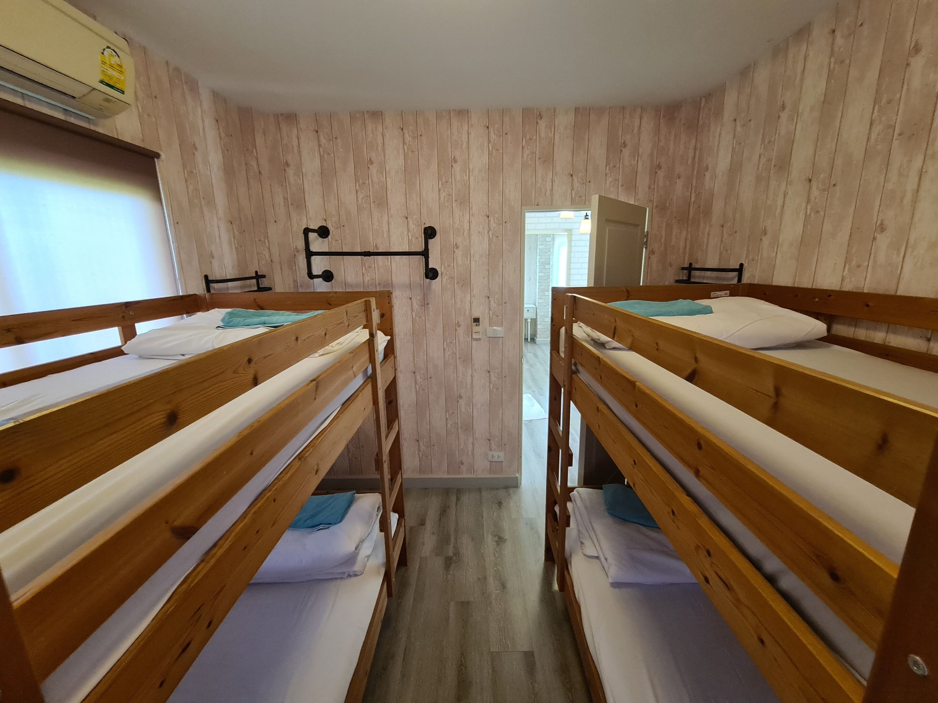 Une pièce avec deux lits superposés en bois, une porte blanche et un climatiseur fixé au mur.