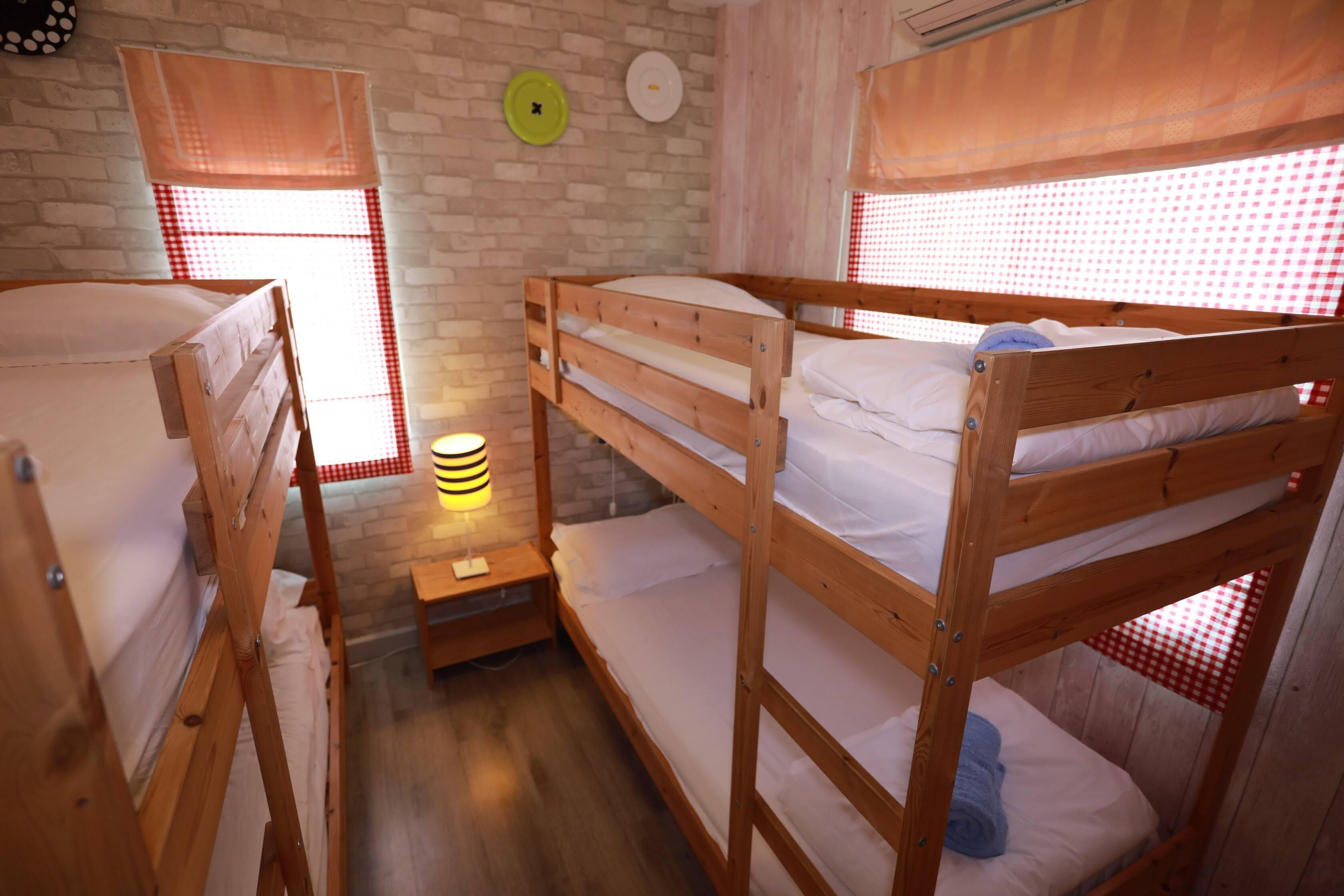 Une chambre avec deux lits superposés, une petite table de chevet avec une lampe et une fenêtre ornée d’un rideau à carreaux.