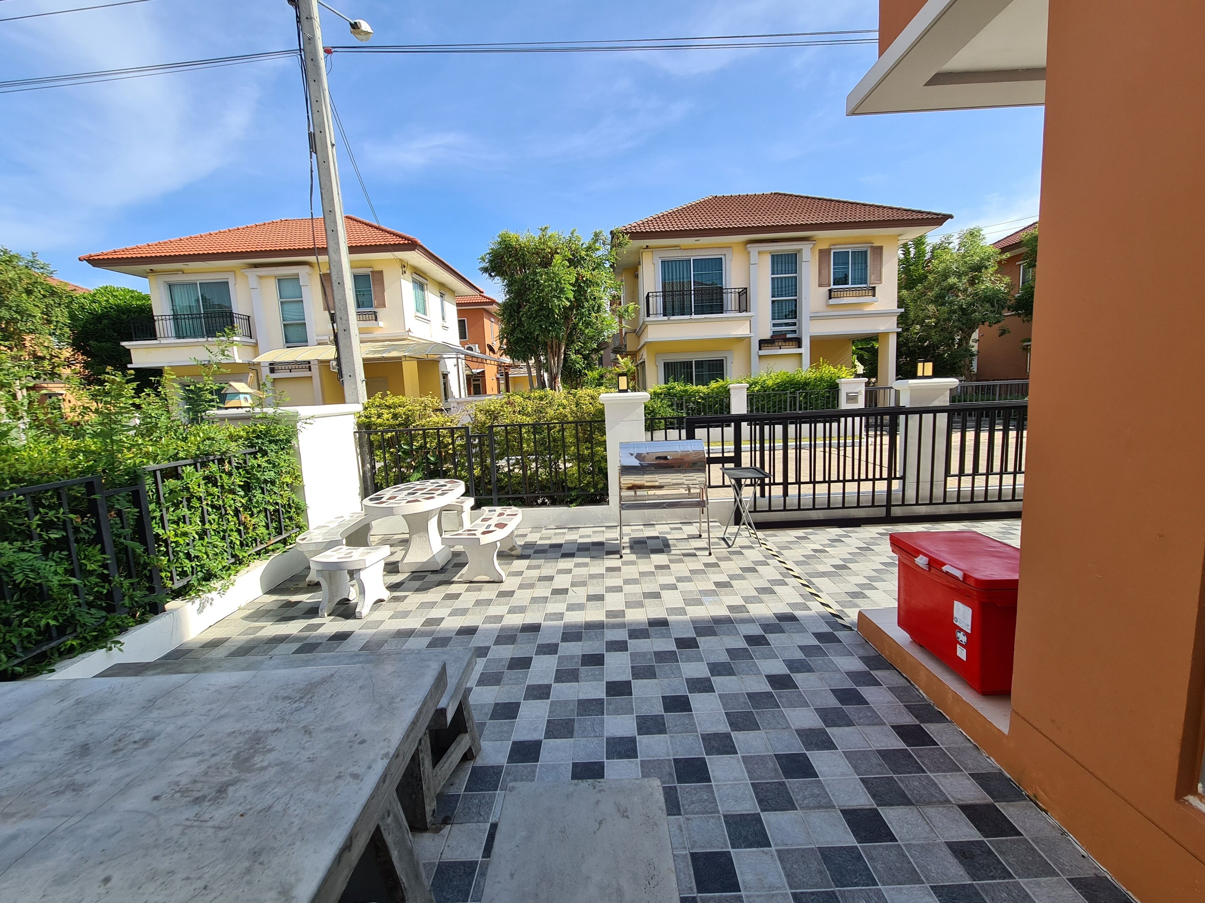 A courtyard with a checkered floor, a small table and chairs, and a red trash bin.