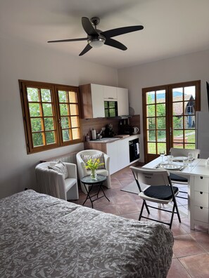 A room with a bed, a desk with a chair, a small table with a vase, a kitchenette, and large windows. - Spacious, 5 bd room home in a beautiful country setting in the French Alps. (Saint-Martin-d'Uriage)