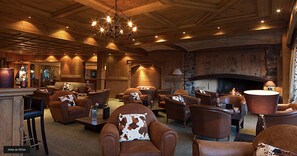 A cozy lobby with leather sofas and armchairs, a grand chandelier, and a stone fireplace. - Apartment Etrier Recently Renovated Crans-montana (Lens)