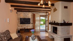 A living room with a stone fireplace, a flat-screen TV, and a sofa with patterned cushions. - Beautiful villa with pool for 8 near the beach (Tar-Vabriga)