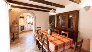 A dining area with a table set for four, wooden chairs, a cabinet with glass doors, and a stone vase on a stand. - Beautiful villa with pool for 8 near the beach (Tar-Vabriga)