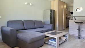 A modern living room with a grey sectional sofa, a small coffee table, and a kitchen area with a fridge and a wooden cabinet. - Renovated studio 4/5 ppl, south balcony, private parking, Pra Loup (Pra-Loup)