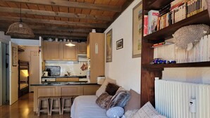 A cozy living room with a sofa, a small kitchen area, and a bookshelf filled with books. - Cozy studio for 4 with sunny terrace in Pra-Loup (Pra-Loup)