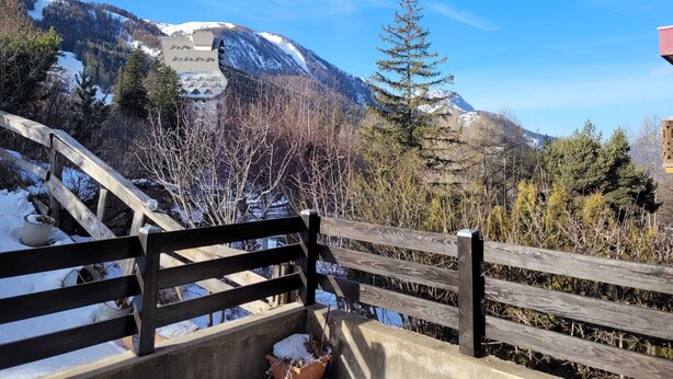 A wooden bridge with a view of a mountain and a building with a snow-covered roof. - Cozy studio for 4 with sunny terrace in Pra-Loup (Pra-Loup)