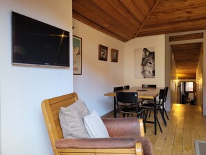 Uma sala de estar acolhedora com teto de madeira, uma TV fixada na parede, um espaço de refeições com mesa e cadeiras, e um quadro grande de um lobo na parede.