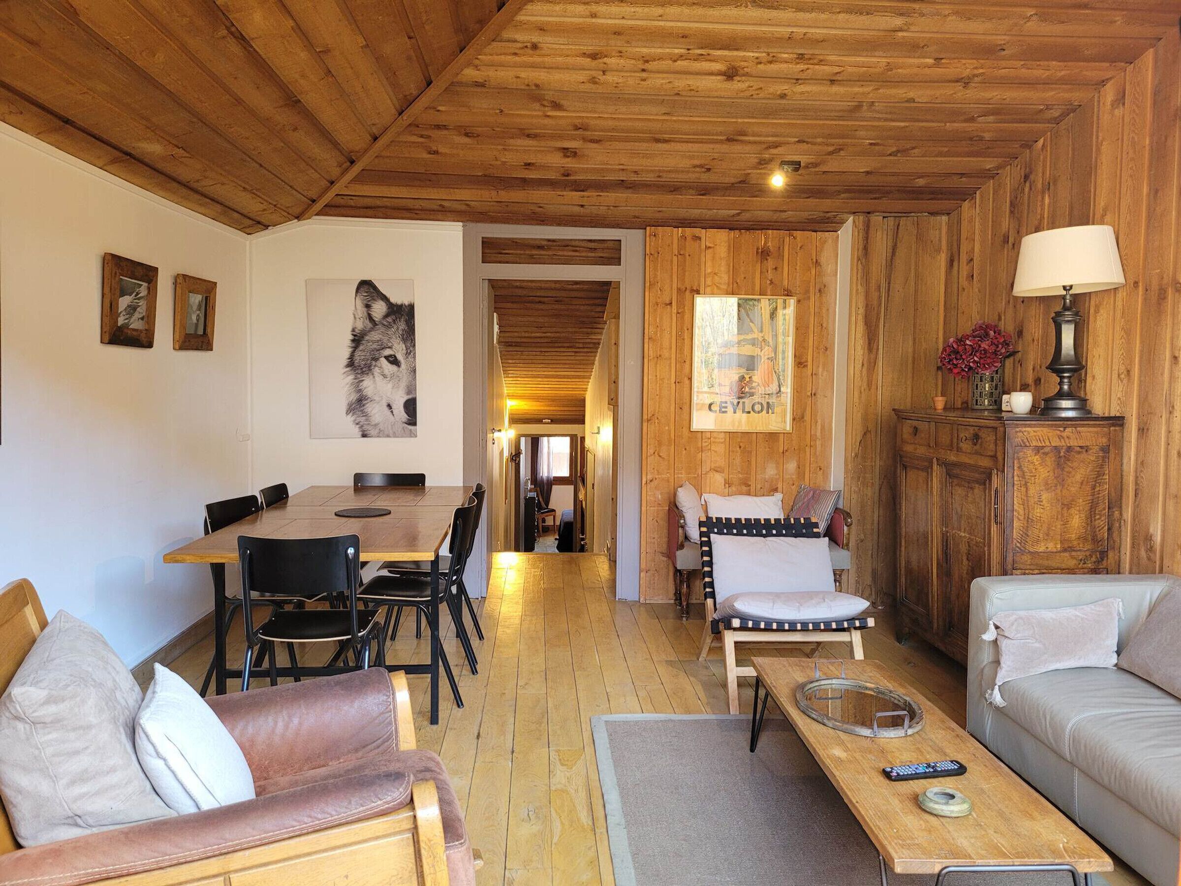 A cozy interior with a wooden ceiling, a dining area with chairs, a sofa, and a coffee table.