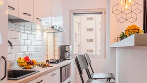 A modern kitchen with white cabinets, a black chair, and a window with a view of buildings. - Studio 54 by MRG Apartments (Bucharest)