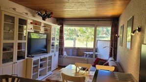 A compact living space with a TV, white cabinets, a dining table, and a view of the outdoors.