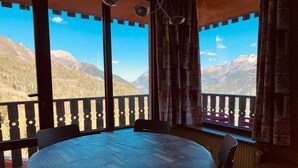A room with a round table, chairs, and a view of mountains through large windows. - Beautiful renovated apartment with private parking in Pra Loup (Pra-Loup)