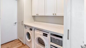 A laundry room with two front-loading washing machines, a white countertop, and white cabinets above.