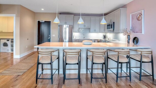 A modern kitchen with a central island, bar stools, pendant lighting, and stainless steel appliances.