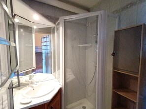 A bathroom with a glass-enclosed shower, a sink with a mirror, and a wooden cabinet.