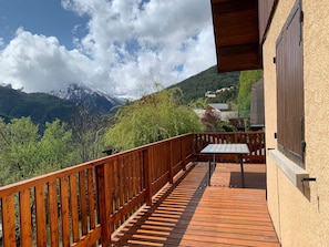 A wooden deck with a table and chairs, overlooking a mountainous landscape with houses in the background.