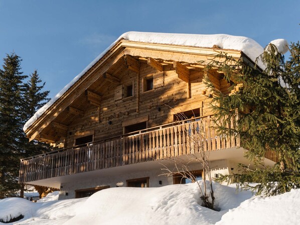 A wooden chalet with a balcony, surrounded by snow and trees.