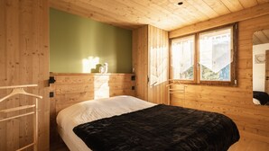 Una habitación tipo cabaña de madera con cama, un armario de madera, un perchero y una ventana con vistas a la montaña.