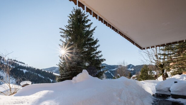 Un muelle cubierto de nieve con baranda de madera, un montículo de nieve y un pino al fondo.