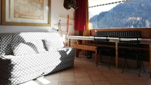 Een gezellige kamer met een gestreept sofa, een houten plafond, een inlijsting kaart aan de muur, een rood gordijn en uitzicht op een bebost gebergte.