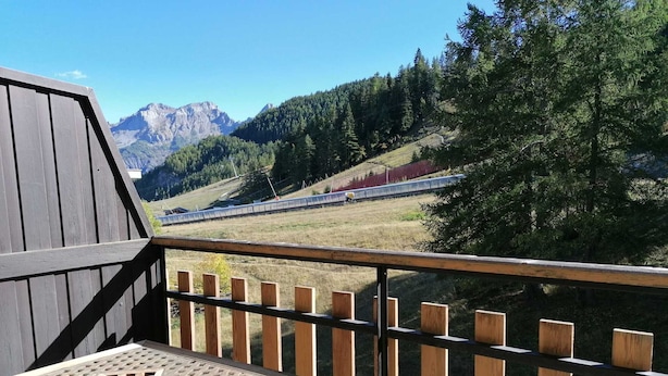 Una terraza de madera con una mesa y una vista a un tren a lo lejos.