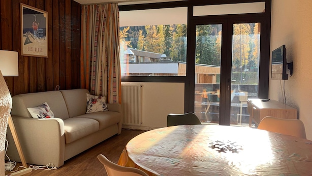 Una habitación acogedora con sofá, una mesa redonda y un ventanal que ofrece vistas a árboles y un edificio.