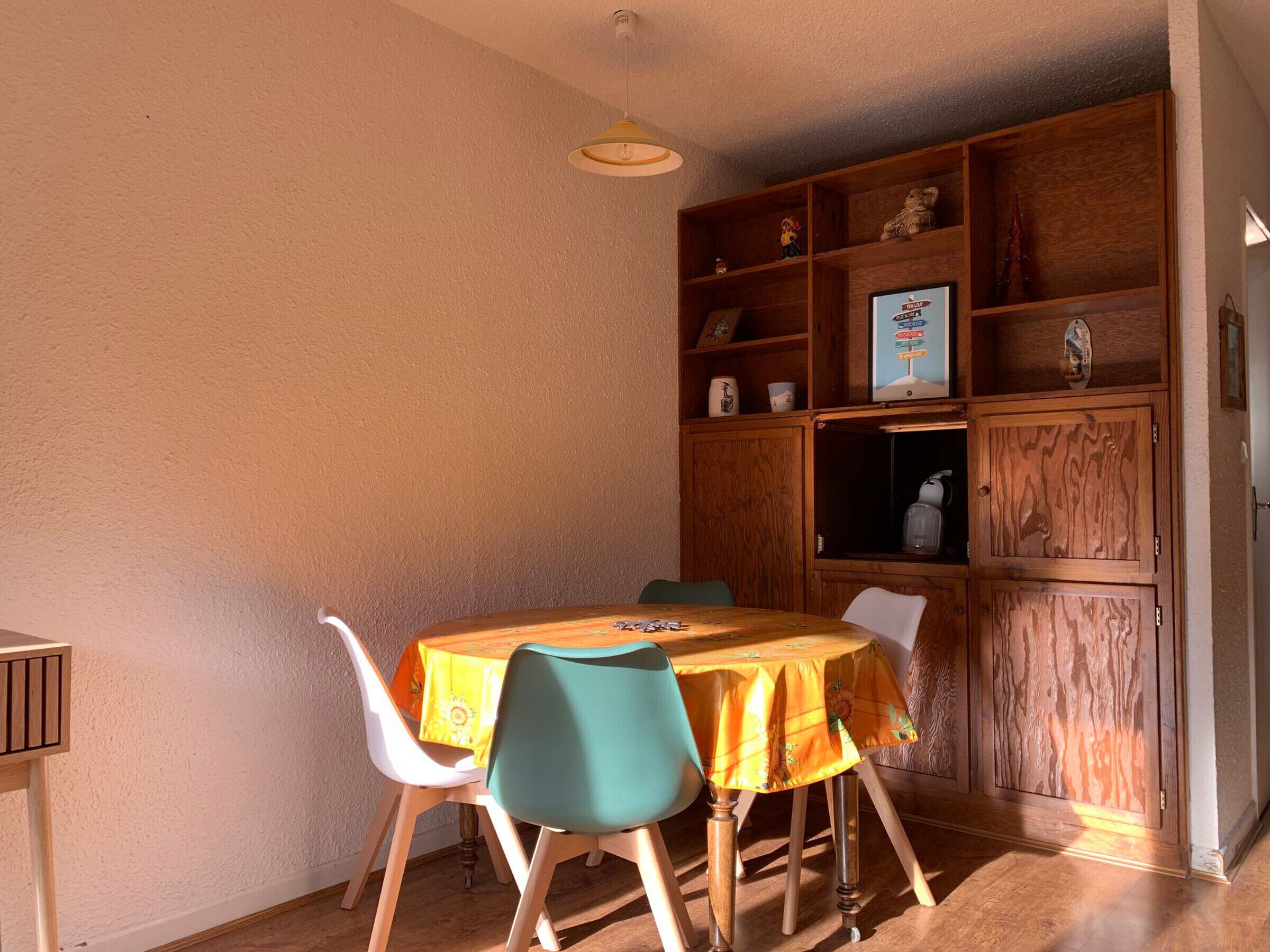 A dining area with a wooden table and chairs, a wooden cabinet with shelves, and a hanging light fixture.