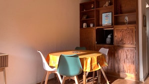 Un comedor con una mesa y sillas de madera, un armario de madera con estantes y una lámpara colgante.