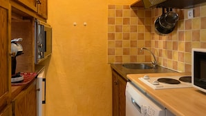 Una cocina compacta con armarios de madera, microondas integrado, estufa y salpicadero de azulejos.