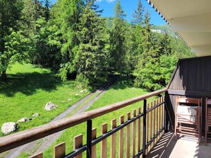 A balcony with a wooden railing overlooking a grassy area with trees and a path. - Renovated 2P apartment on slopes, calm in Pra Loup (Pra-Loup)