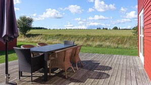 Um deck de madeira com uma mesa e cadeiras de vime, com vista para um campo.
