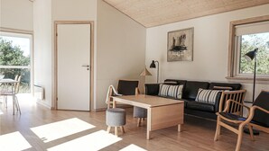 Uma sala de estar moderna com piso de madeira, um sofá de couro preto, uma mesa de centro de madeira e uma área de jantar com mesa e cadeiras.