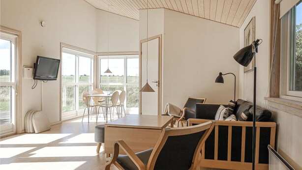 Um quarto espaçoso com uma mesa de jantar de madeira, cadeiras, um sofá e uma TV fixada na parede.