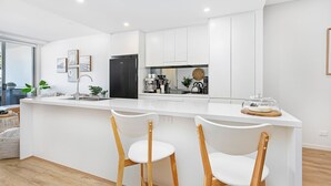 Uma cozinha moderna com ilha central, armários brancos e duas cadeiras de madeira.