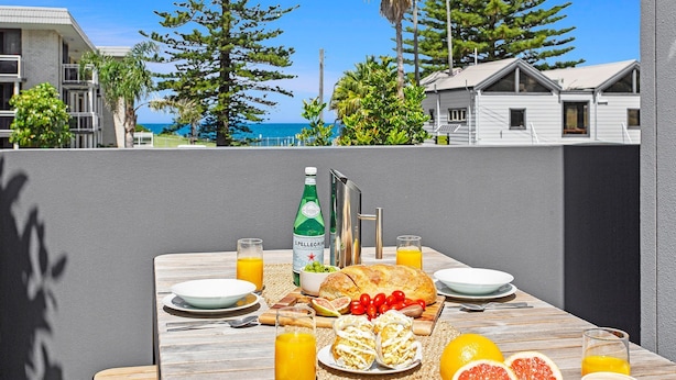 Mesa posta para o pequeno-almoço com vista para o oceano, incluindo uma garrafa de água Pellegrino, pão, tomates e frutas cítricas.