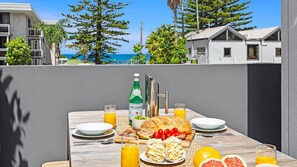 Una mesa lista para el desayuno con vista al océano, que incluye una botella de agua Pellegrino, pan, tomates y frutas cítricas.
