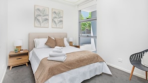 Quarto moderno com uma cama grande, duas mesas de cabeceira, um criado-mudo, uma cadeira e uma janela com vista para o verde.