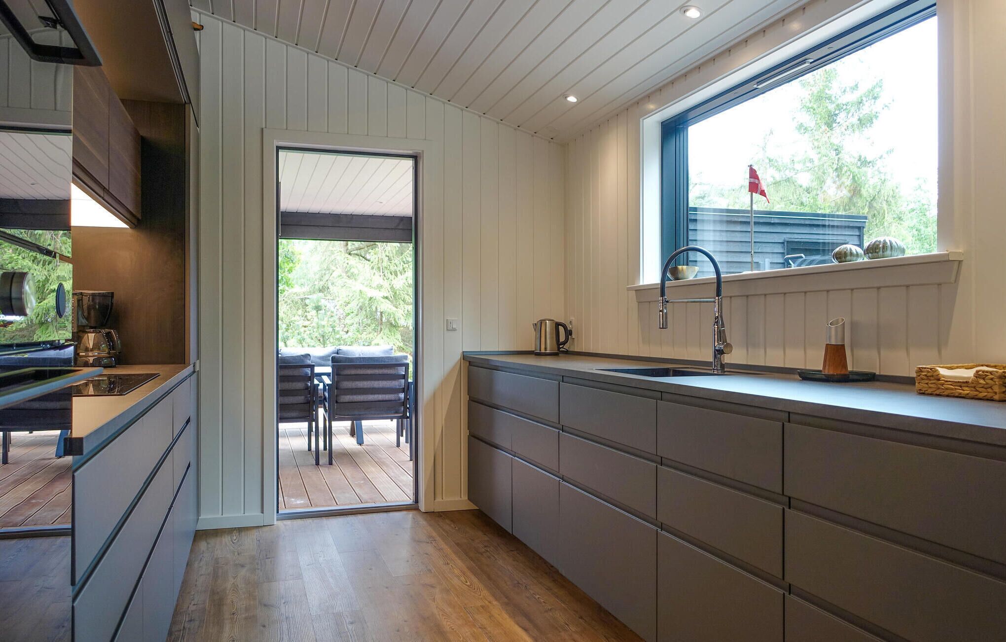 A modern kitchen with a large window, wooden flooring, and a view of outdoor seating.