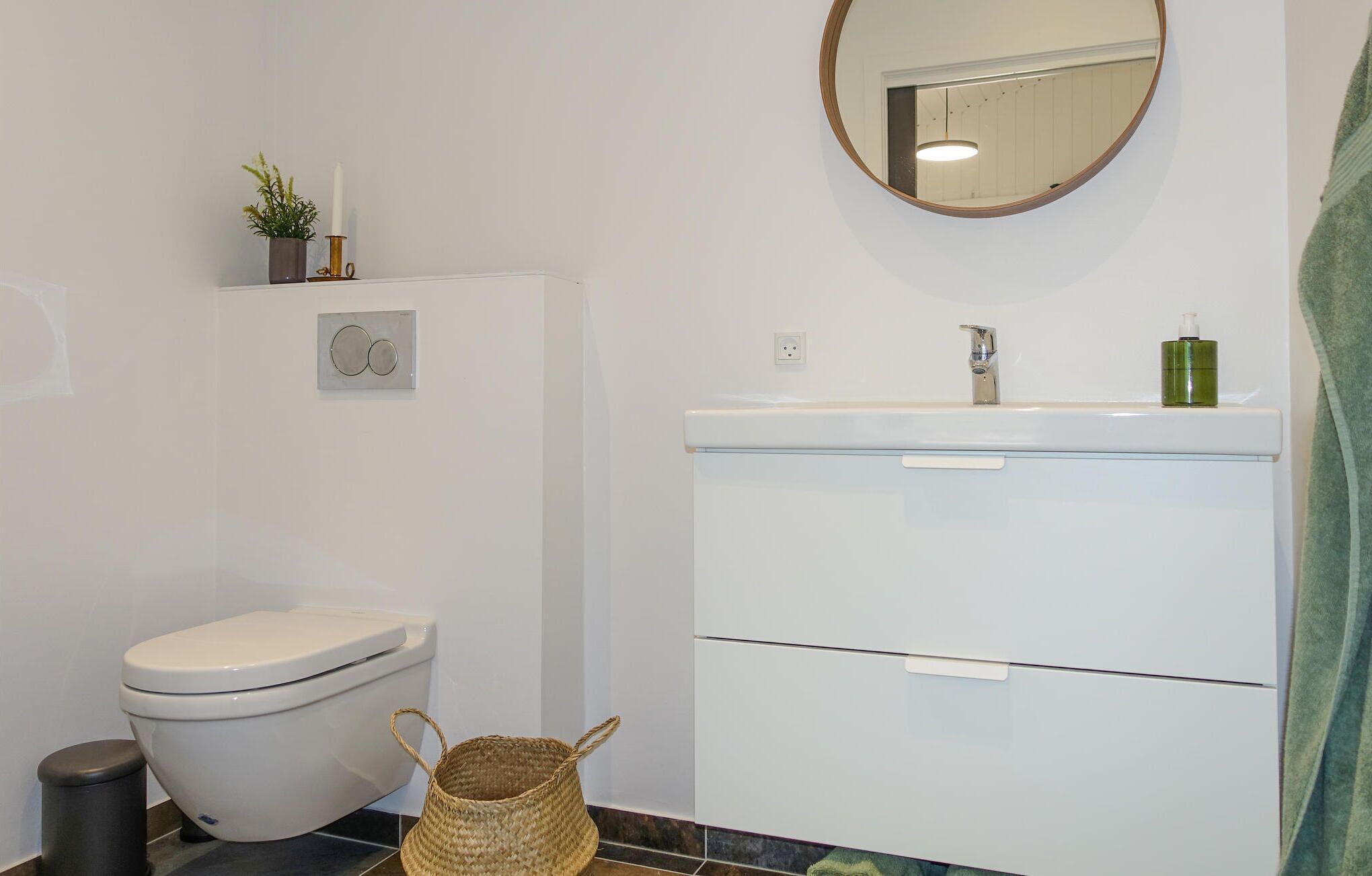 Un baño con inodoro, lavamanos con espejo y un cubo de basura.